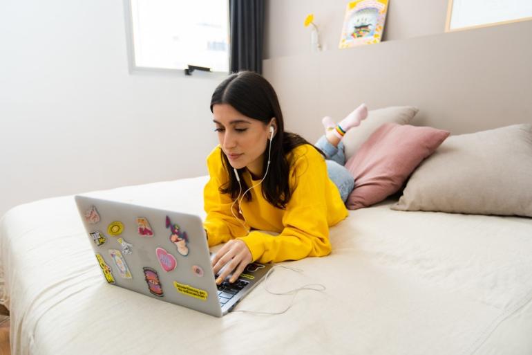 Mujer acostada en una cama y usando un computador portátil 